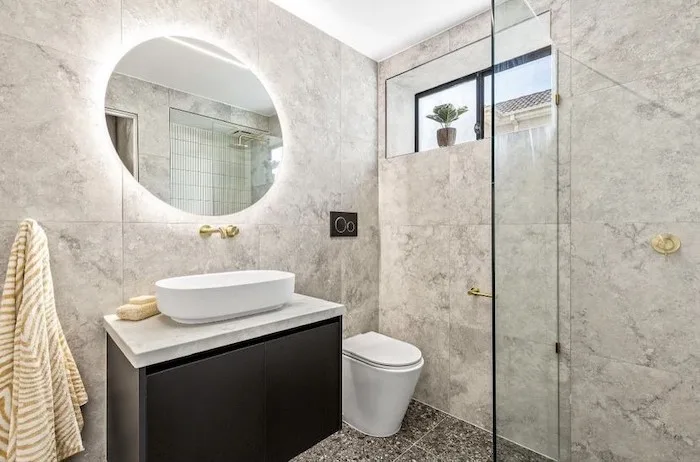 Marble-look bathroom with backlit round mirror